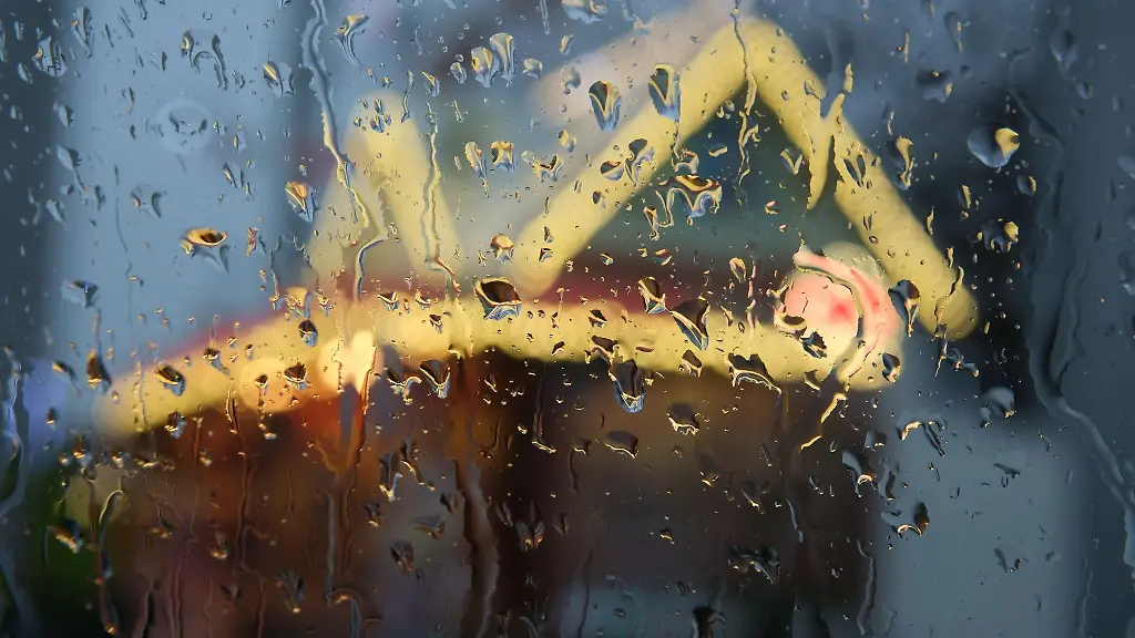 Ein-beleuchteter-Stand-auf-einem-Weihnachtsmarkt-ist-durch-eine-regennasse-Fensterscheibe-zu-sehen