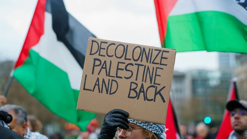 Eine-Kundgebungsteilnehmerin-haelt-ein-Schild-Decolonize-Palestine-Land-Back-hoch