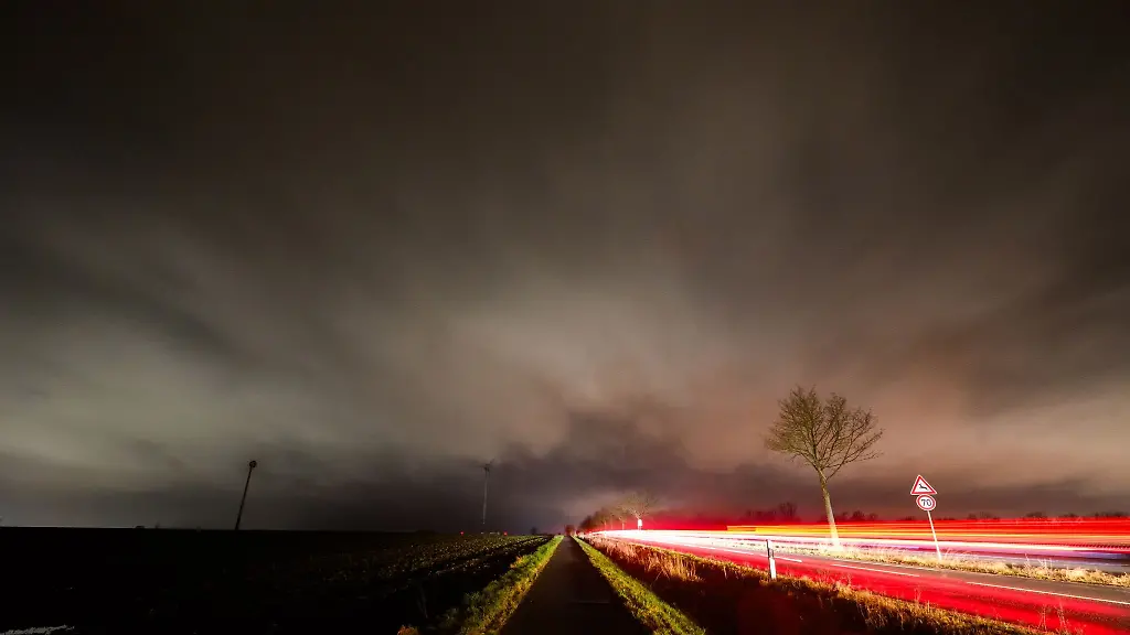Wolken-ziehen-ueber-eine-Landschaft-hinweg-waehrend-Autos-ueber-eine-Landstrasse-fahren