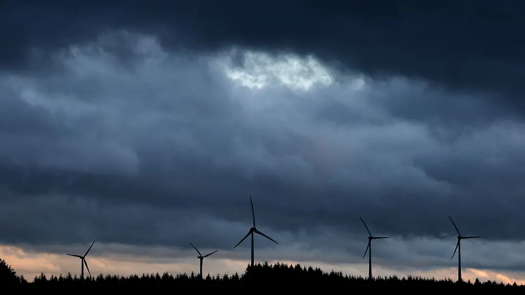 Windraeder-stehen-unter-dichten-Regenwolken-hinter-einem-Wald