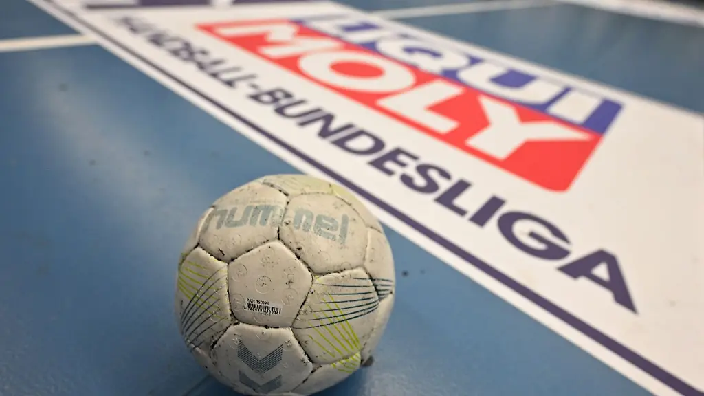 Ein-Handball-liegt-auf-dem-Boden-dahinter-ist-das-Logo-der-Handball-Bundesliga-HBL-zu-sehen