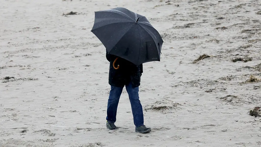 Ein-Spaziergaenger-geht-bei-Regen-und-Wind-an-einem-Strand-entlang