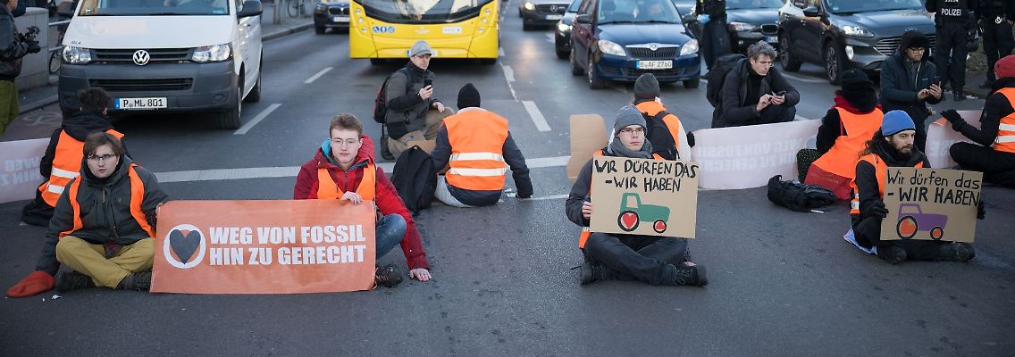 Aktivisten der Klimaschutzgruppe Letzte Generation sitzen bei einer Straßenblockade auf der Straße.