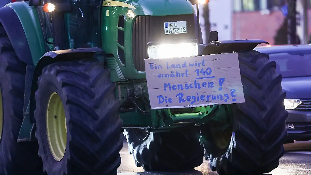 Einer-von-mehreren-Landwirten-faehrt-mit-seinem-Traktor-und-einem-Plakat-durch-denBerufsverkehr
