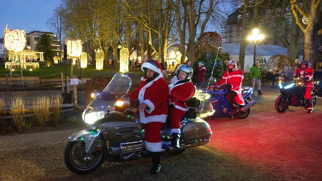 Die-Riding-Santas-Weihnachtsmaenner-auf-bunt-beleuchteten-Motorraedern-im-Kurpark