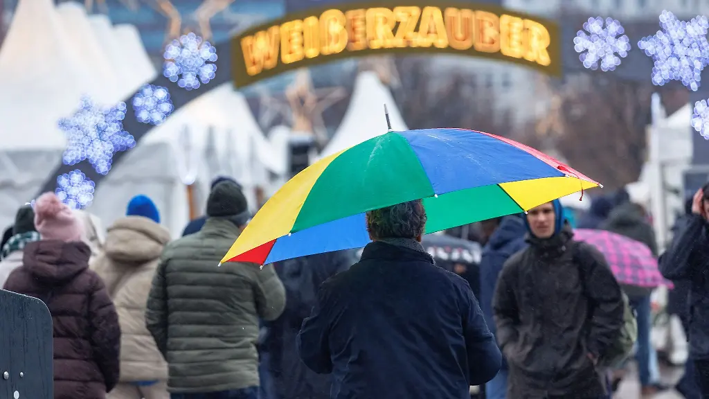 Ein-Mann-geht-im-Nieselregen-mit-seinem-Schirm-ueber-einen-Weihnachtsmarkt