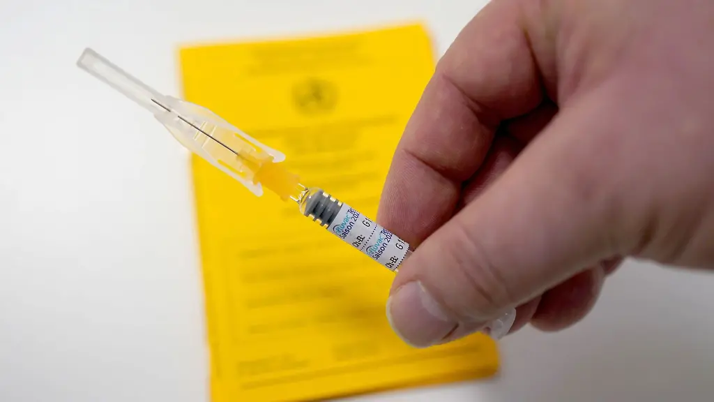 Ein-Arzt-haelt-eine-Spritze-mit-dem-Grippeschutzimpfstoff-Influvac-Tetra-ueber-einen-Impfausweis