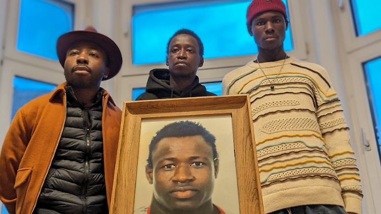 William Dountio, Sidy Dramé, Lassana Dramé (v.l.n.r.) mit einem Bild ihres getöteten Bruders. 