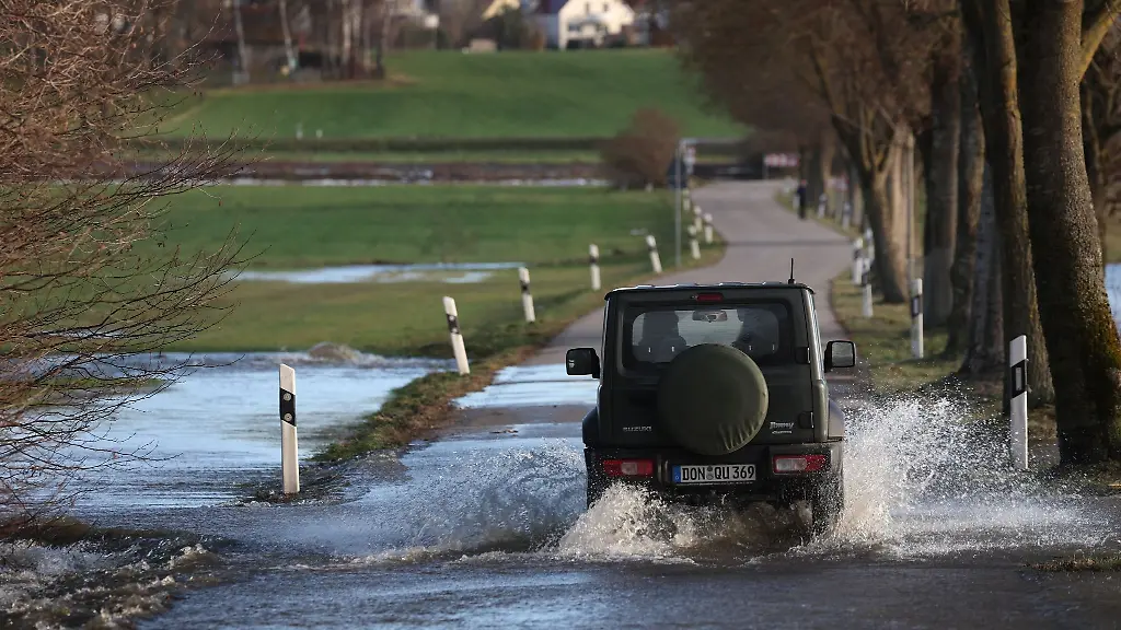 Ein-Auto-faehrt-auf-einer-vom-Hochwasser-der-Schmutter-ueberfluteten-Strasse