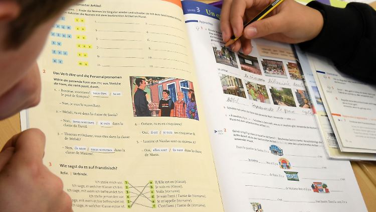 Schülerinnen und Schüler arbeiten mit einem Lehramtsstudenten im Lehrbuch Französisch.