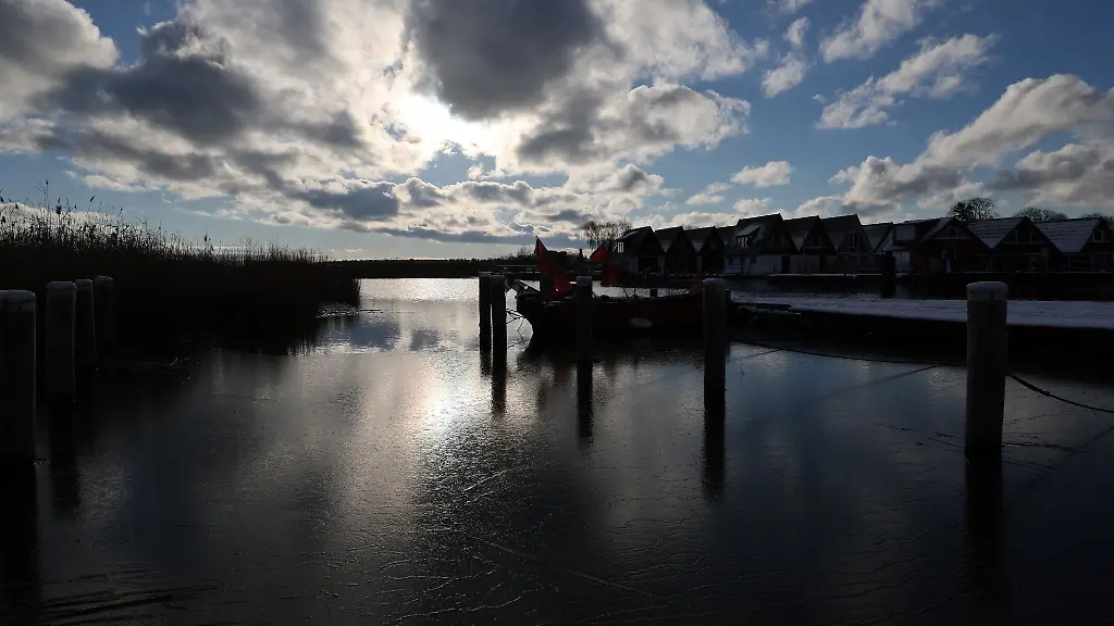 Ueber-dem-schneebedeckten-Boddenhafen-spiegeln-sich-Sonne-und-Wolken-in-der-duennen-Eisschicht