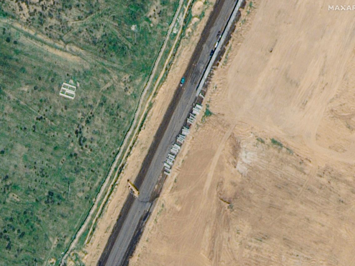 Stark vergrößert: Am Rand einer planierten Fläche entsteht aus Betonfertigteilen eine Mauer.
