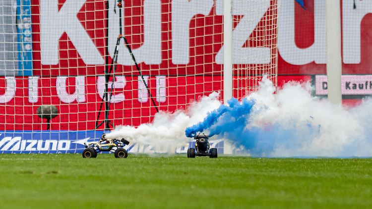 Zwei Autos fahren in Rostock über das Spielfeld.