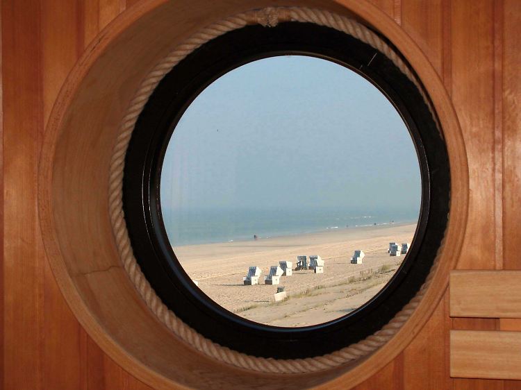 Innen heiß und draußen kalt: Im Winter fällt der Blick aus dem Bullauge der Strandsauna auf leere Strandkörbe und die graue Nordsee.