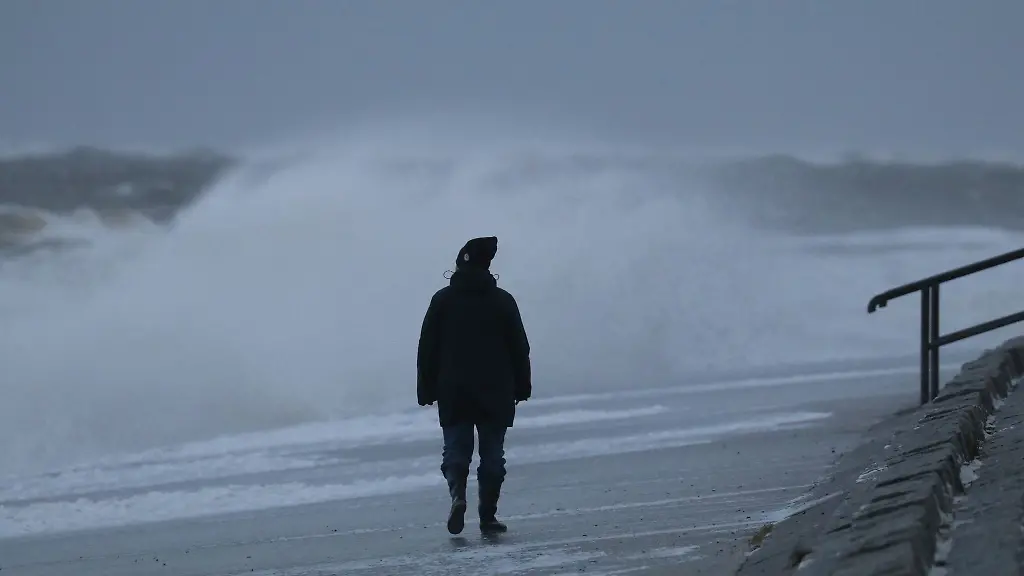 Eine-Spaziergaengerin-laeuft-bei-stuermischem-Wetter-am-Nordstrand-der-ostfriesischen-Insel-Norderney