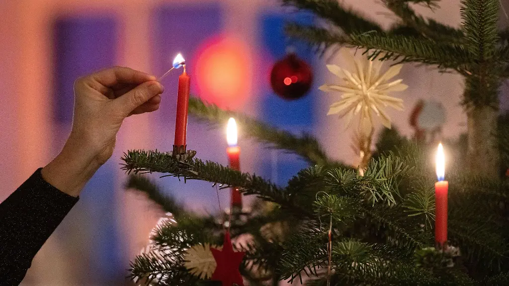 Eine-Frau-zuendet-eine-Kerze-an-einem-Weihnachtsbaum-an