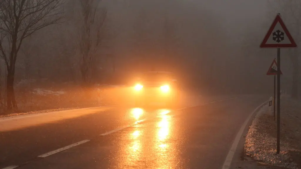 Ein-Auto-faehrt-bei-Glatteis-und-Nebel-ueber-eine-Strasse