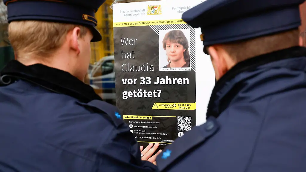 Polizisten-haengen-das-Plakat-zum-Cold-Case-von-Claudia-Obermeier-an-einer-Glasscheibe-auf