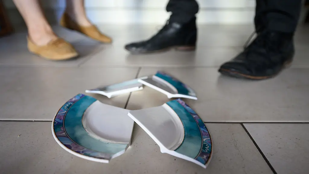 Ein-Mann-und-eine-Frau-stehen-hinter-einem-zerbrochenen-Teller-in-einer-Kueche