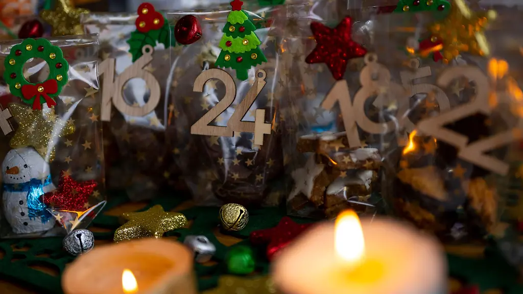 Ein-selbstgemachter-Adventskalender-mit-kleinen-Tueten-steht-neben-zwei-Kerzen-auf-einem-Tisch