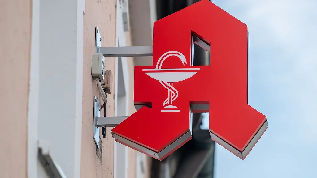 Ein-Schild-mit-dem-Apotheken-Logo-haengt-an-einer-Hauswand