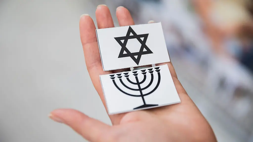 Eine-Frau-haelt-die-Karten-eines-Memory-Spiels-mit-einem-Davidstern-sowie-einer-Menora-in-der-Hand