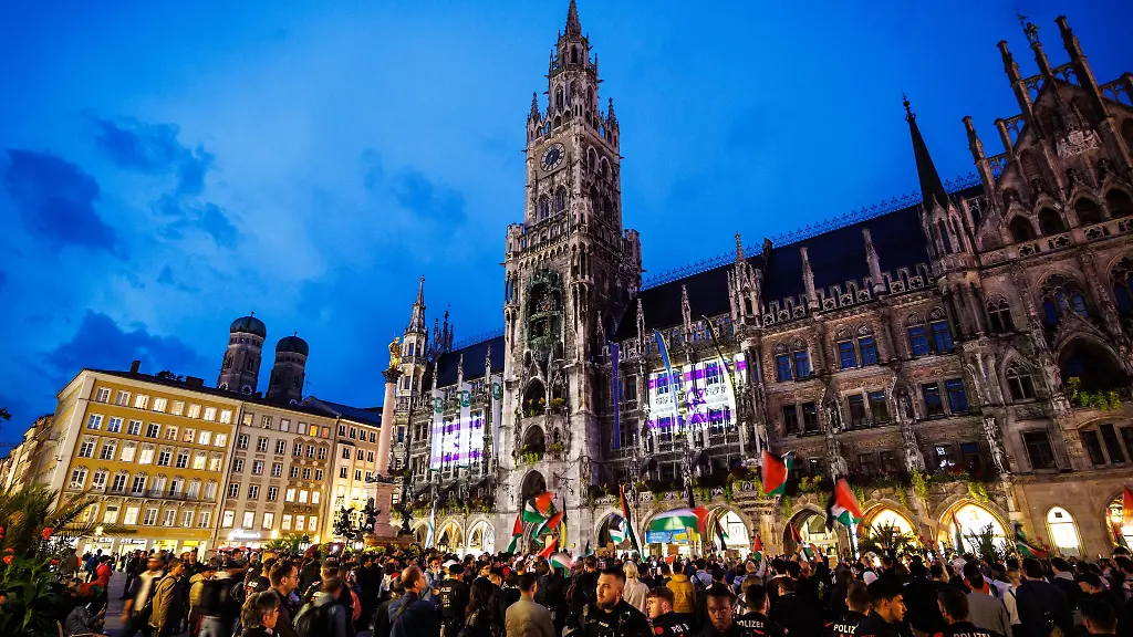 Die-israelische-Flagge-ist-auf-dem-Rathaus-am-Marienplatz-zu-sehen-waehrend-Menschen-an-einer-Kundgebung-teilnehmen