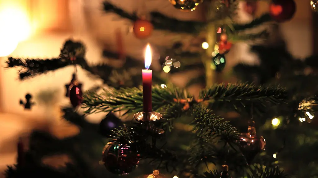 Eine-Kerze-brennt-an-einem-festlich-geschmueckten-Weihnachtsbaum