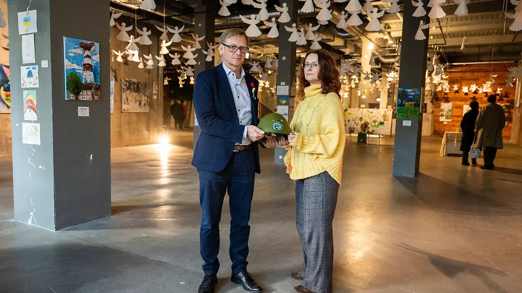 Tetyana-Sell-r-und-Oleg-Motus-stehen-in-einer-Ausstellung-mit-Malereien-von-Kindern-aus-befreiten-ukrainischen-Staedten