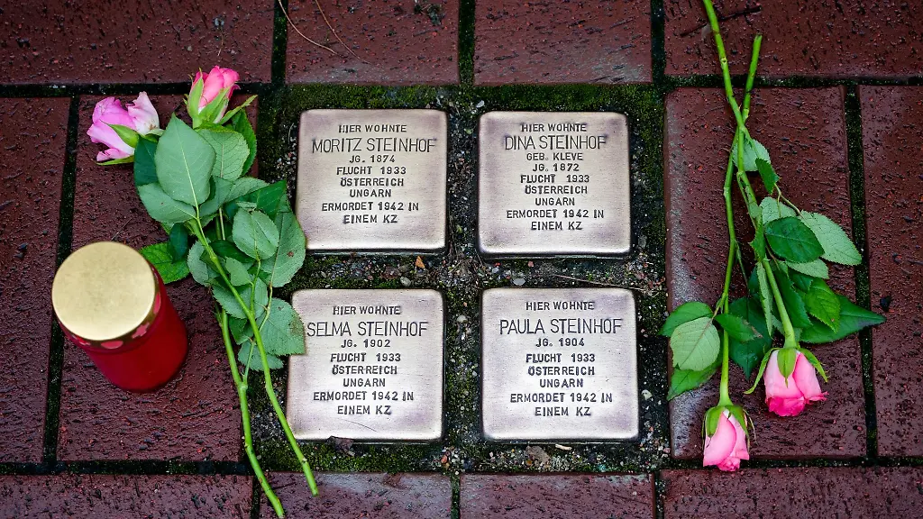 Rosen-und-Kerzen-liegen-und-stehen-neben-geputzten-Stolpersteinen-fuer-Opfer-des-Nationalsozialismus