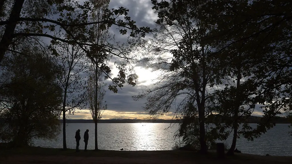 Ausfluegler-beobachten-am-Ufer-des-im-Sonnenschein-glitzernden-Ammersees-eine-Ente