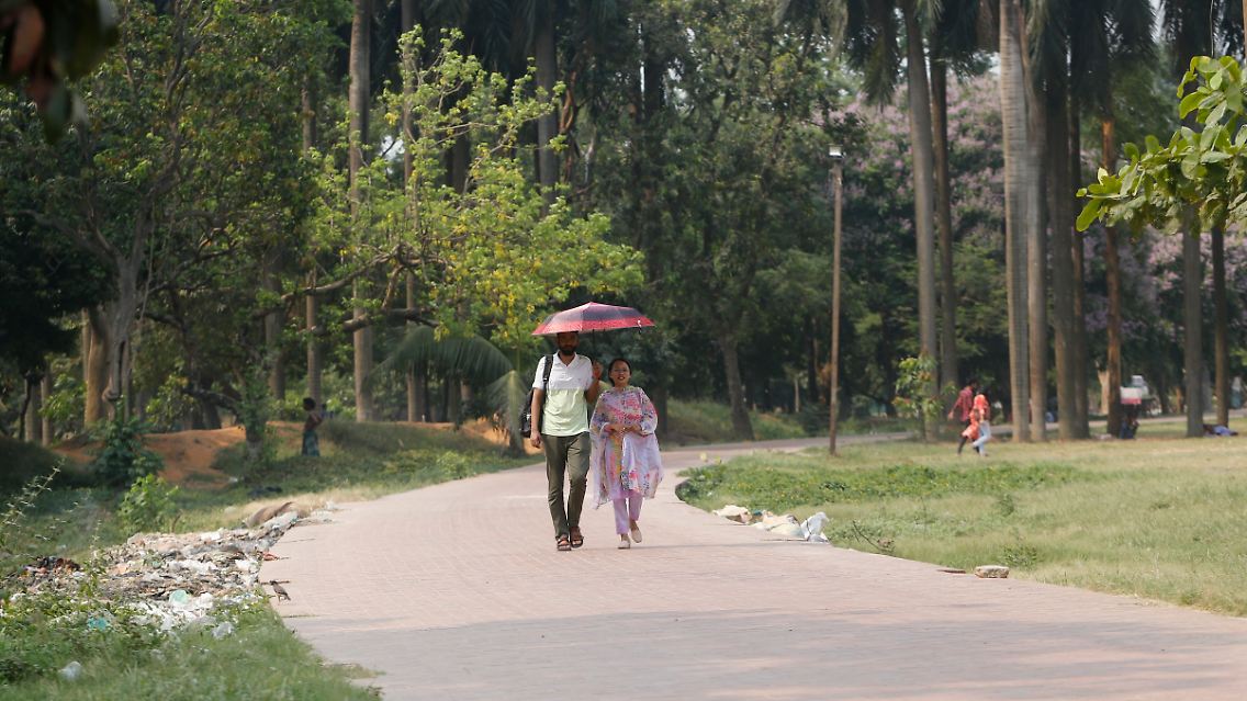 Beim Spaziergang in einem Park in Dhaka hält ein Mann einen Schirm als Schutz vor der Sonne.