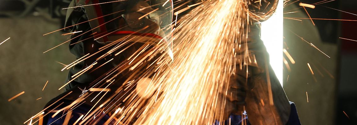 Ein Mitarbeiter eines Maschinenbauers schneidet mit einem Trennschleifer korrodierte Metallteile aus dem Träger in einem Wagenkasten.