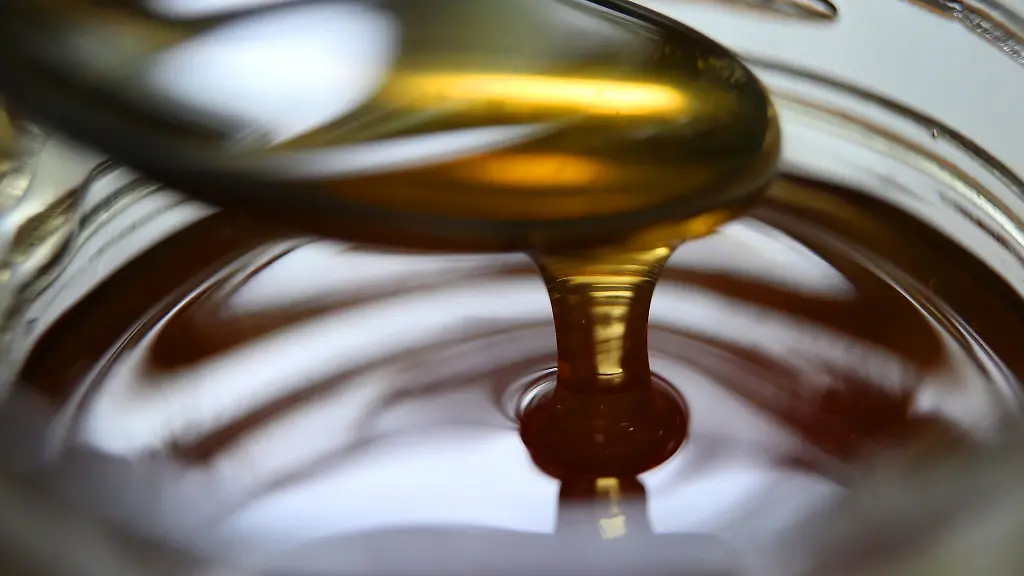 Honig-fliesst-von-einem-Loeffel-in-ein-Honigglas