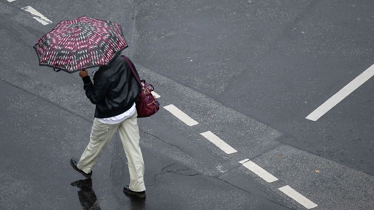 Mit einem Schirm schützt sich eine Passantin vor dem strömenden Regen.