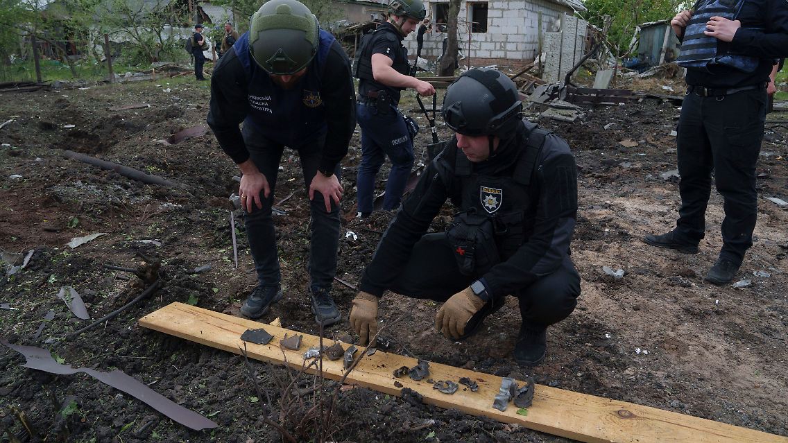 Ein ukrainischer Polizeibeamter und ein Staatsanwalt für Kriegsverbrechen inspizieren Bruchstücke einer Gleitbombe vor einem beschädigten Haus nach einem russischen Luftangriff auf ein Wohnviertel in der ostukrainischen Großstadt Charkiw.