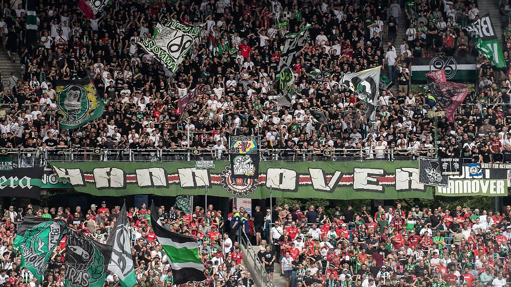 Fans-von-Hannover-96-stehen-mit-Fahnen-auf-der-Tribuene
