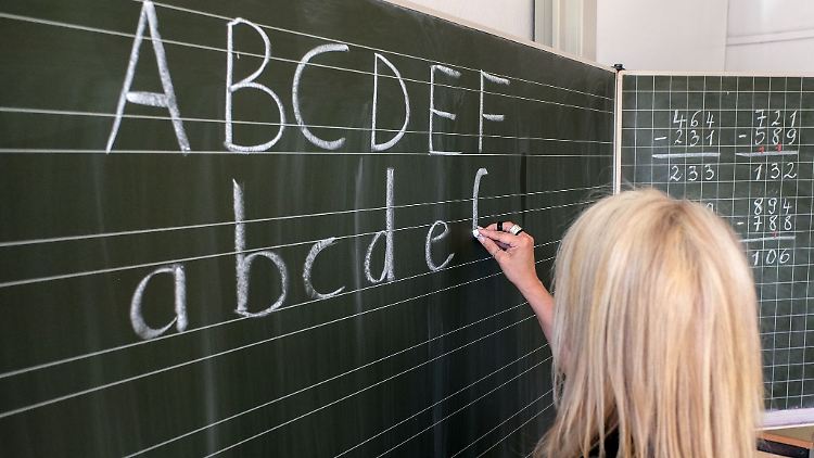 Eine Grundschullehrerin schreibt die ersten Buchstaben des Alphabets auf eine Schultafel in einem Klassenzimmer.