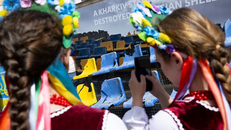 Zwei Frauen fotografieren bei einer Kundgebung in München Fußballsitze aus dem von russischen Angriffen zerstörten Stadion in Charkiw.