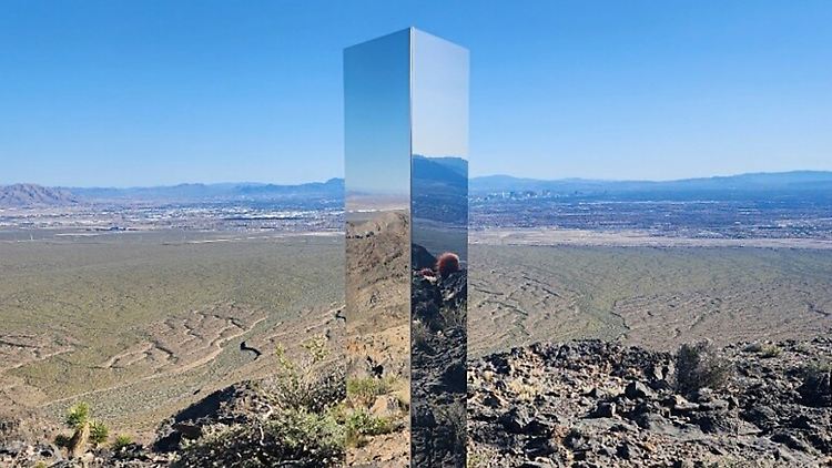 In der metallischen Stele spiegeln sich umliegendes Geröll und Gestrüpp wider.