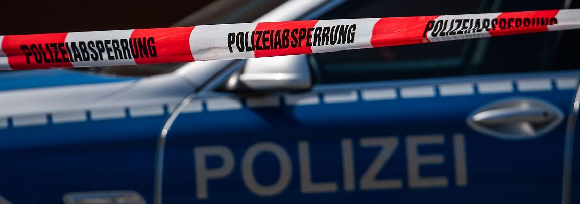 Ein Polizeiauto steht hinter einem Absperrband der Polizei.