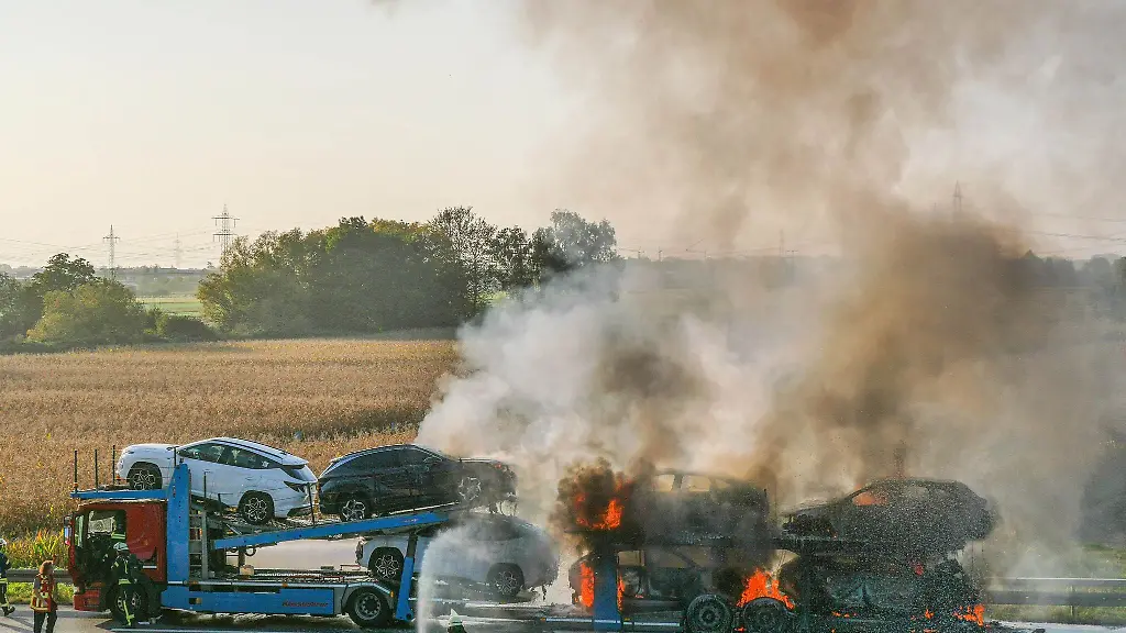 Einsatzkraefte-der-Feuerwehr-loeschen-in-Brand-geratene-Autos-auf-einem-Transporter