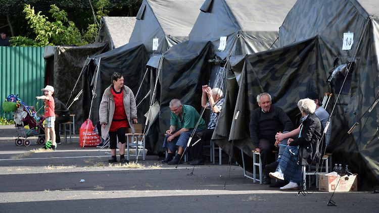 Menschen, die in der Region Kursk evakuiert wurden, sitzen neben Zelten in einem provisorischen Aufenthaltszentrum. 