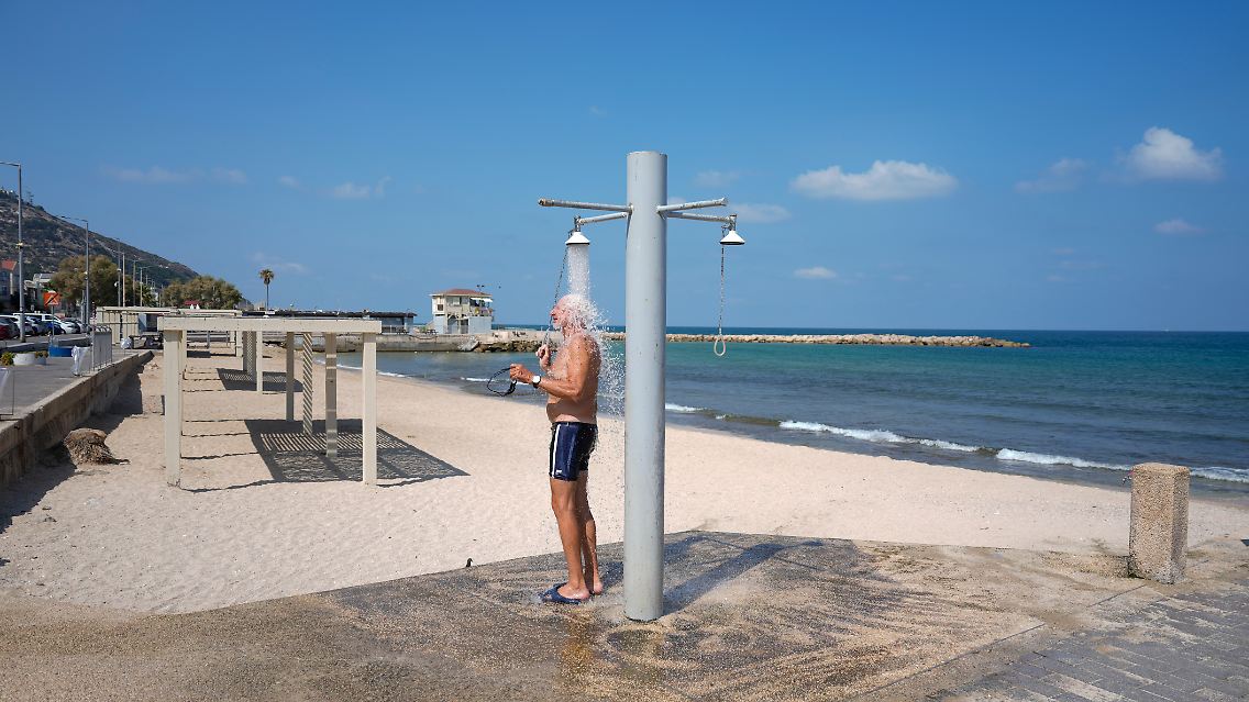 Ein Mann duscht einsam an einem Strand von Haifa.