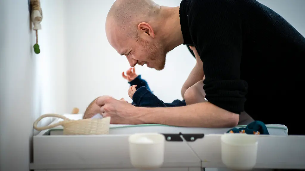 Ein-frisch-gebackener-Vater-beugt-sich-ueber-sein-Baby-das-auf-einem-Wickeltisch-liegt