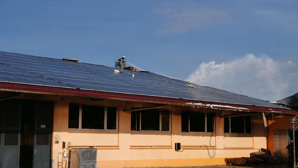 Ein-Feuerwehrmann-loescht-einen-Brand-an-einer-Photovoltaikanlage-auf-dem-Dach-eines-Gebaeudes-der-Ersten-Markgraefler-Winzergenossenschaft