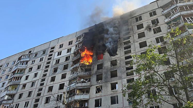 Nach dem Einschlag steigen Flammen aus dem mehrstöckigen Wohnhaus auf.