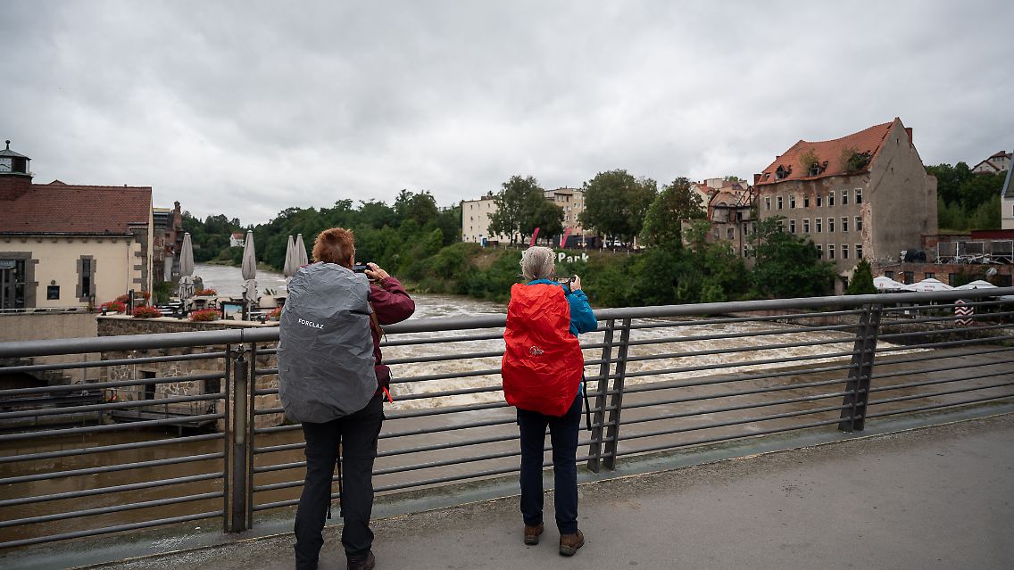 Zwei Passantinnen fotografieren das Hochwasser der Neiße auf der Altstadtbrücke in Görlitz. Auch an der Neiße in Görlitz ist Alarmstufe 2 erreicht, dort liegt der Wasserstand bei 4,42 Metern.