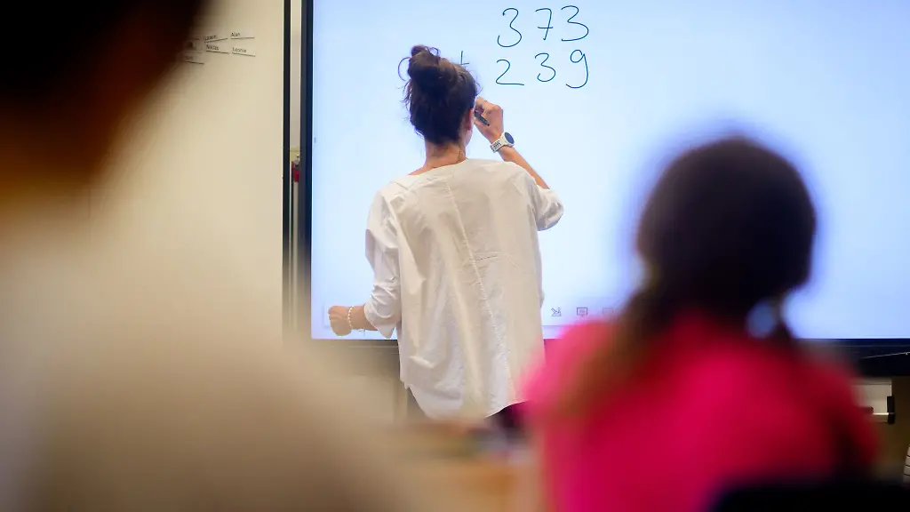 Ein-Lehrerin-schreibt-eine-Mathematikaufgabe-auf-eine-digitale-Schultafel-im-Klassenraum-einer-4