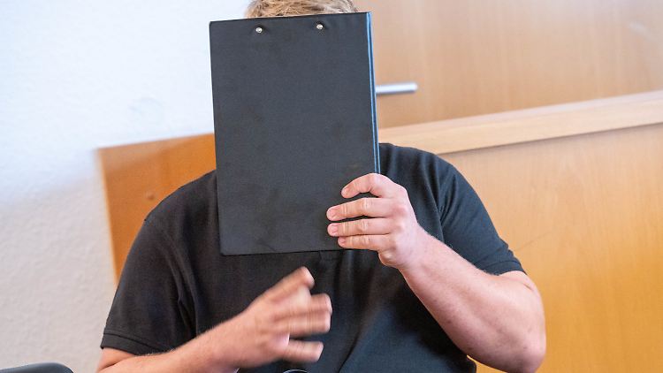 Der Angeklagte hält im Sitzungssaal im Amtsgericht einen Schreibblock vor sein Gesicht.